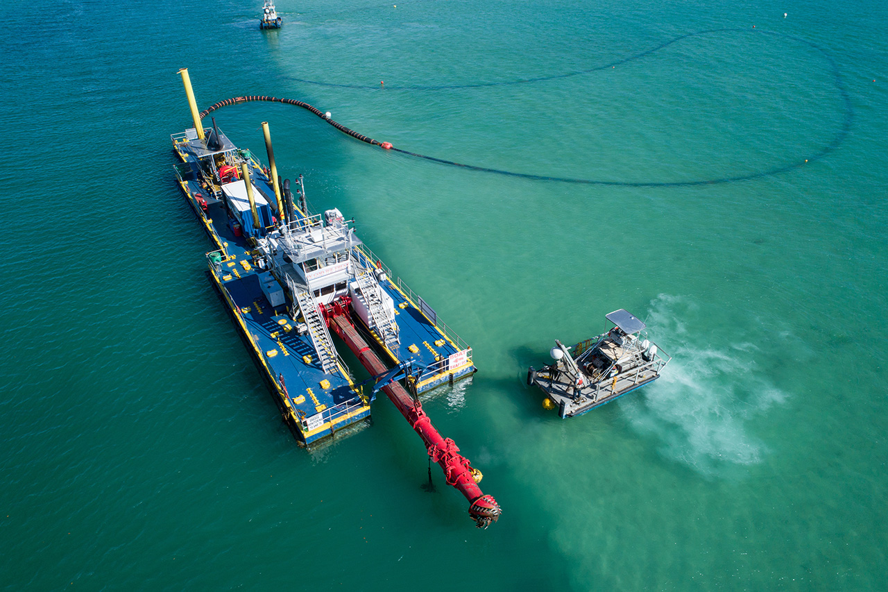 ship engaged in the dredging process with a slurry hose attached to the back of the craft.