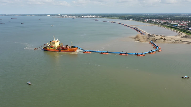 Dredging vessel pumping dredged material via floating pipeline